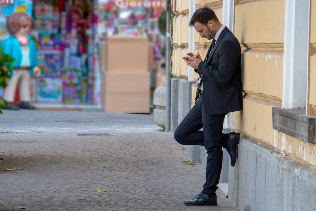 A man checking his phone while leaning on a building — the moment a local query lands and gets answered by rank or by citation