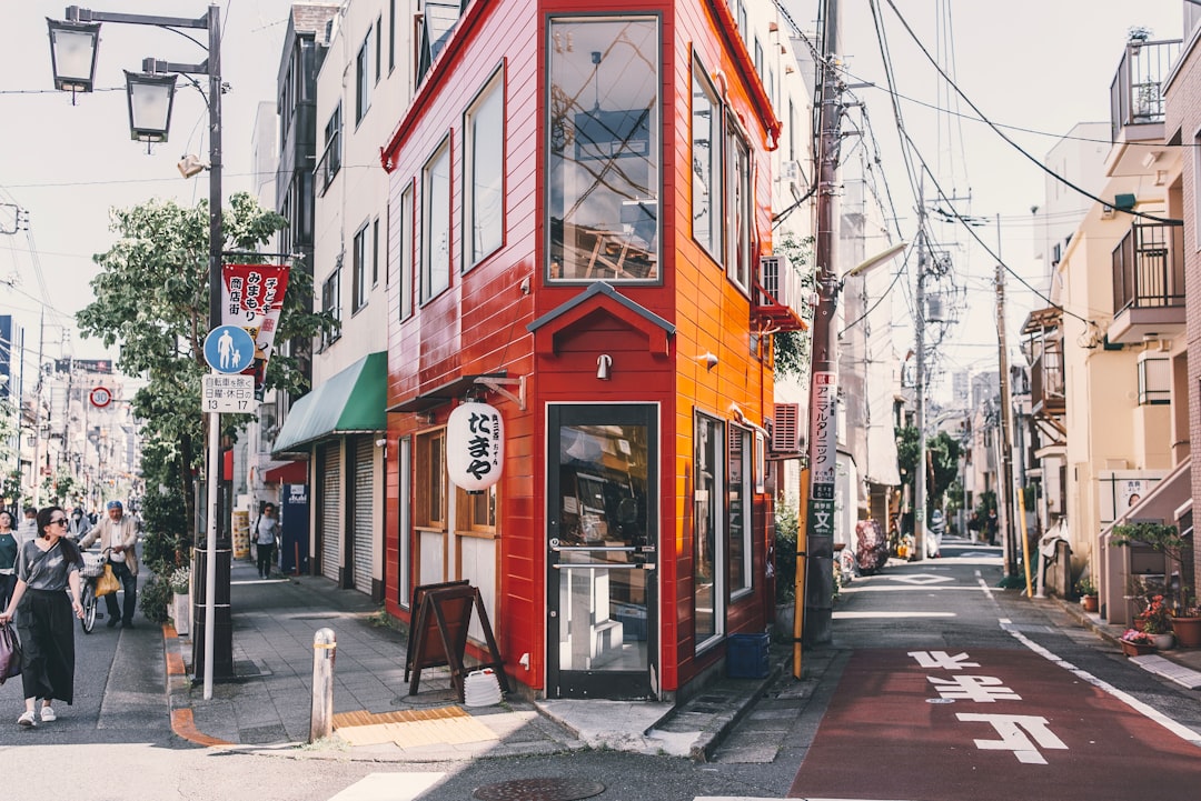 赤い建物の前を歩く女性。街の一角に一つだけ存在する単店舗の見立て — 一つの物理店舗が一つの JSON-LD entity に射影される 1:1 mapping